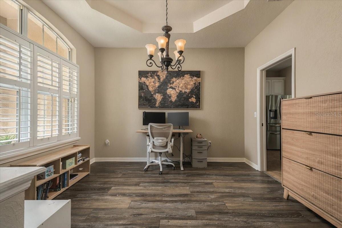 Home office with a dual-monitor desk beneath a world map, beside arched shuttered windows.