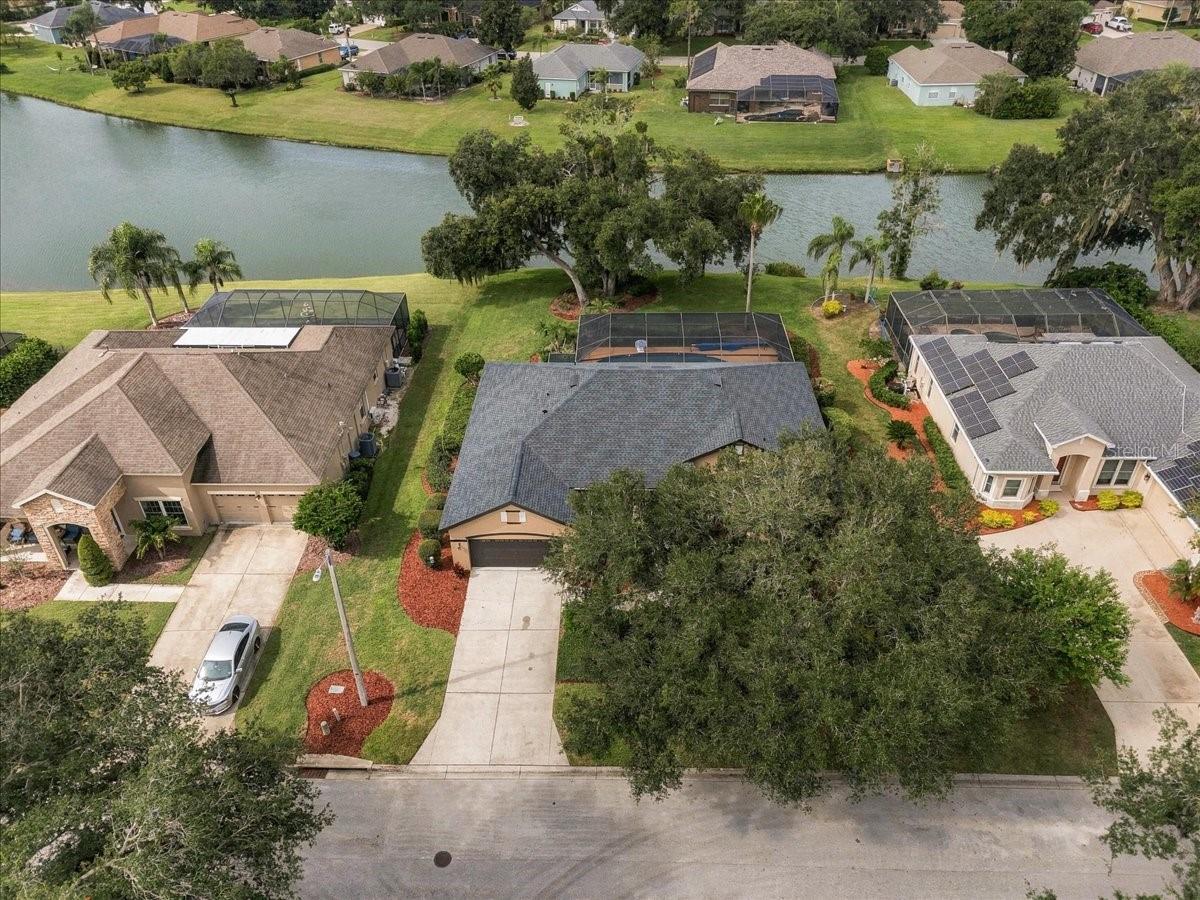 Aerial view of a lakeside home and neighboring properties, with screened pools and mature trees.