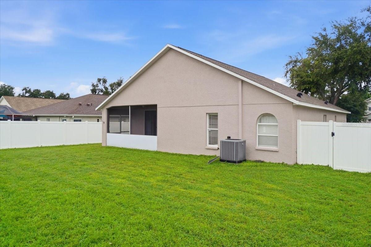 Rear exterior of a beige home with a screened lanai and fenced green lawn.
