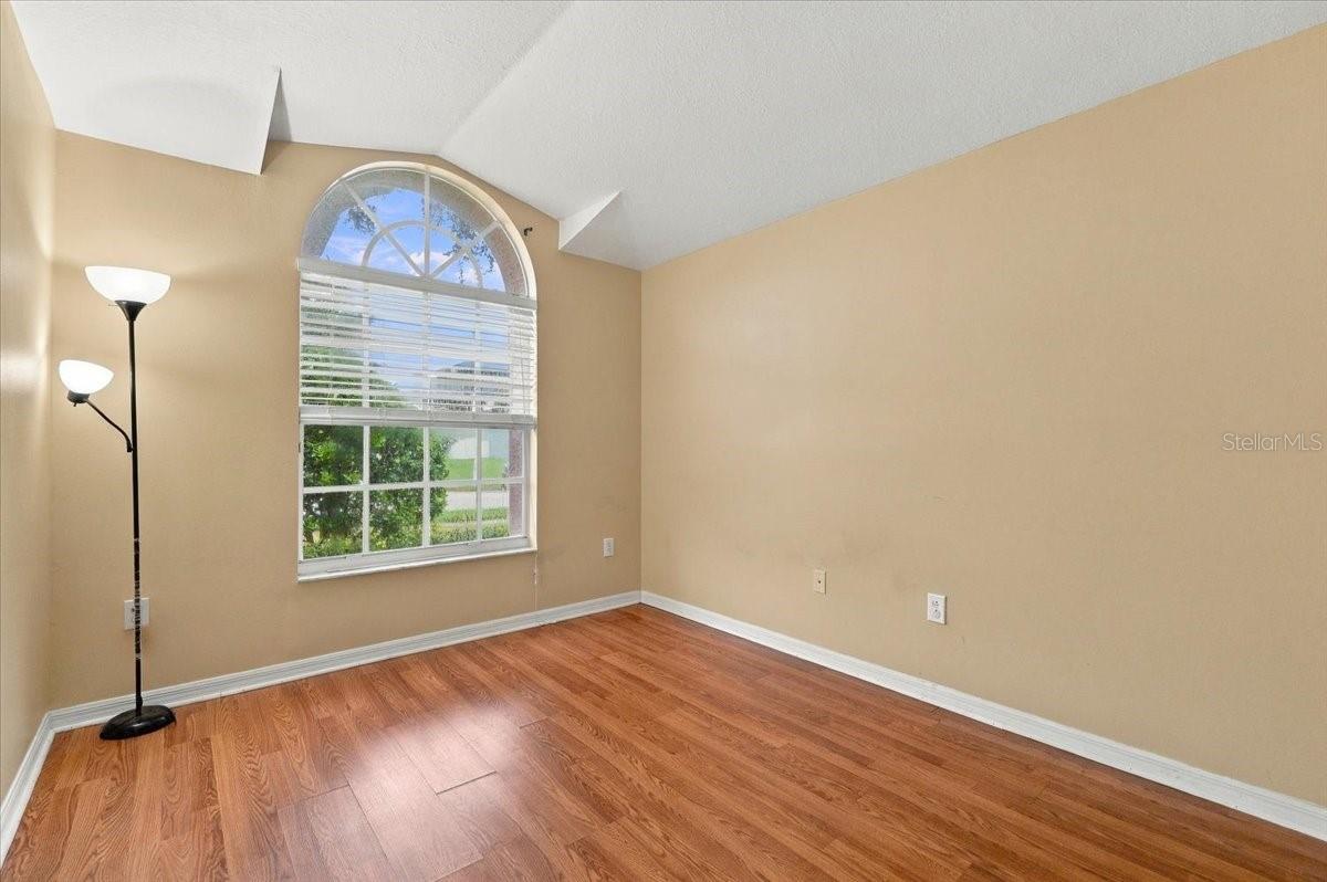 Empty room with warm wood flooring, beige walls, and a large arched window with blinds.