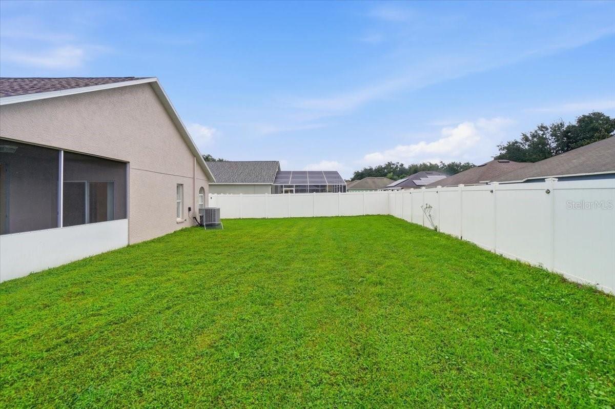 Fenced backyard with a broad green lawn beside the house and screened porch.