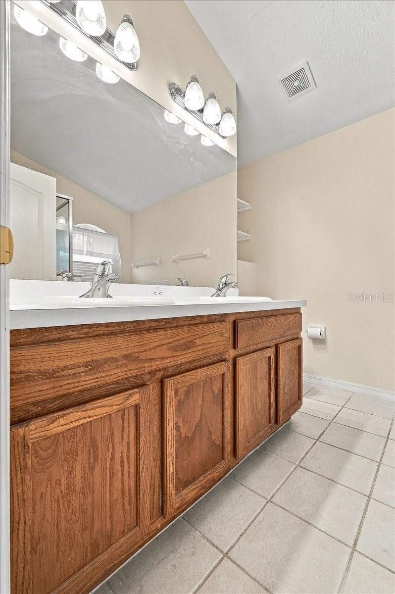 Bathroom vanity with oak cabinets, a long white countertop, and a large mirror.