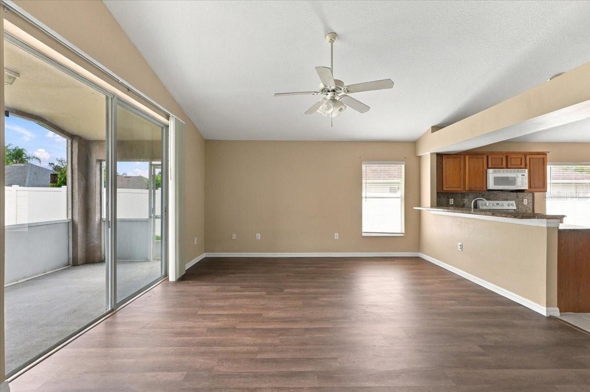 Empty living and dining area with wood-look flooring, sliding patio doors, and an open kitchen.