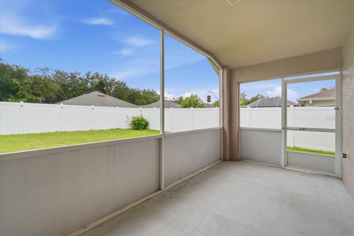 Screened patio with a concrete floor, white privacy fence, and grassy backyard.