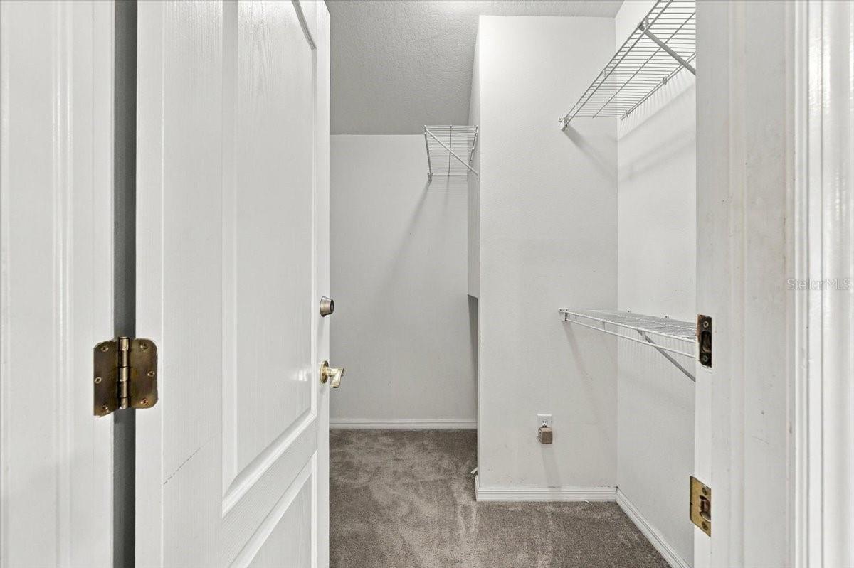 Empty walk-in closet with gray carpet and white wire shelving.