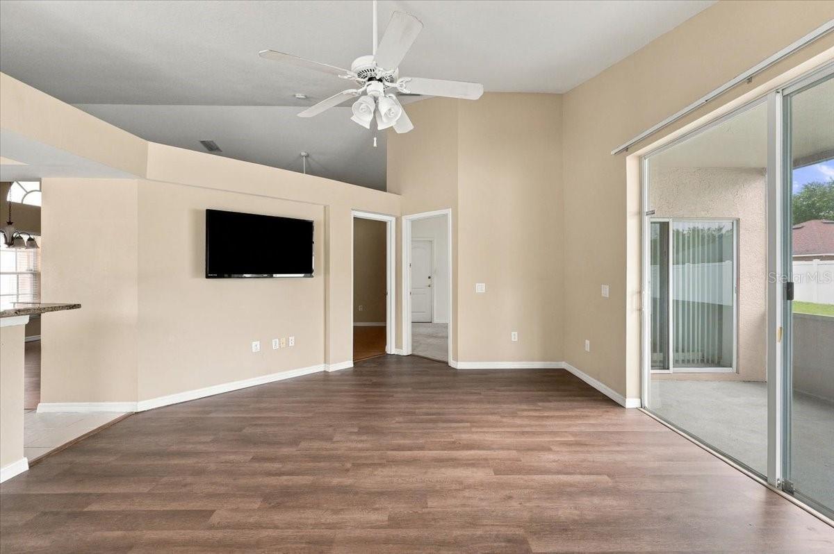Empty living room with vaulted ceiling, mounted television, and sliding glass doors to the patio.