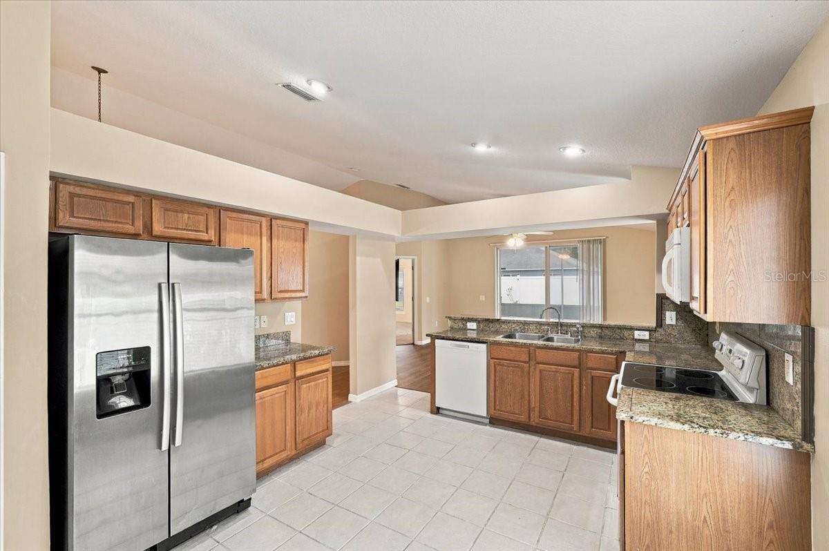 Kitchen with oak cabinets, granite counters, stainless steel refrigerator, and tiled floors.