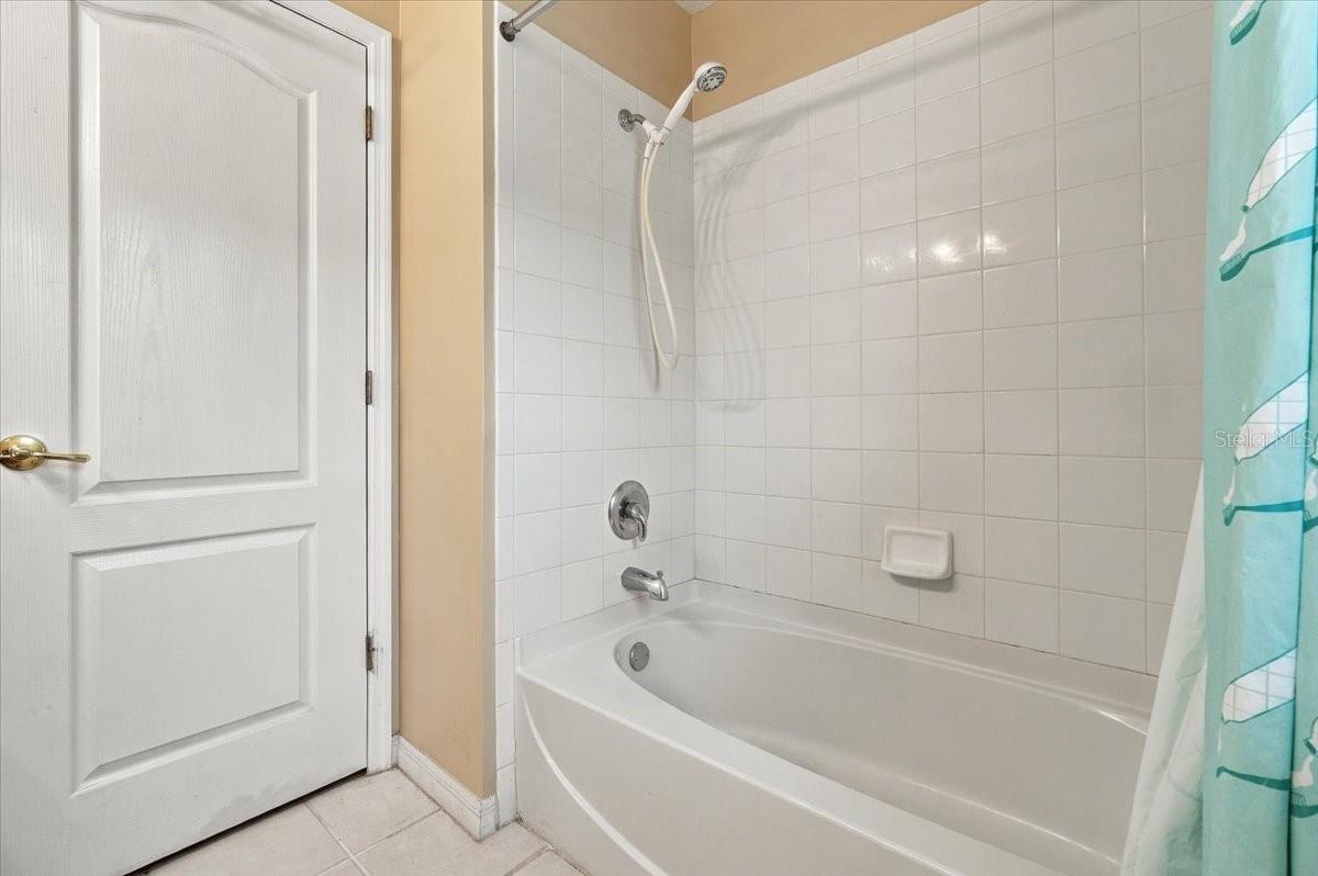 Bathroom with a white tiled tub and shower, handheld showerhead, and turquoise curtain.