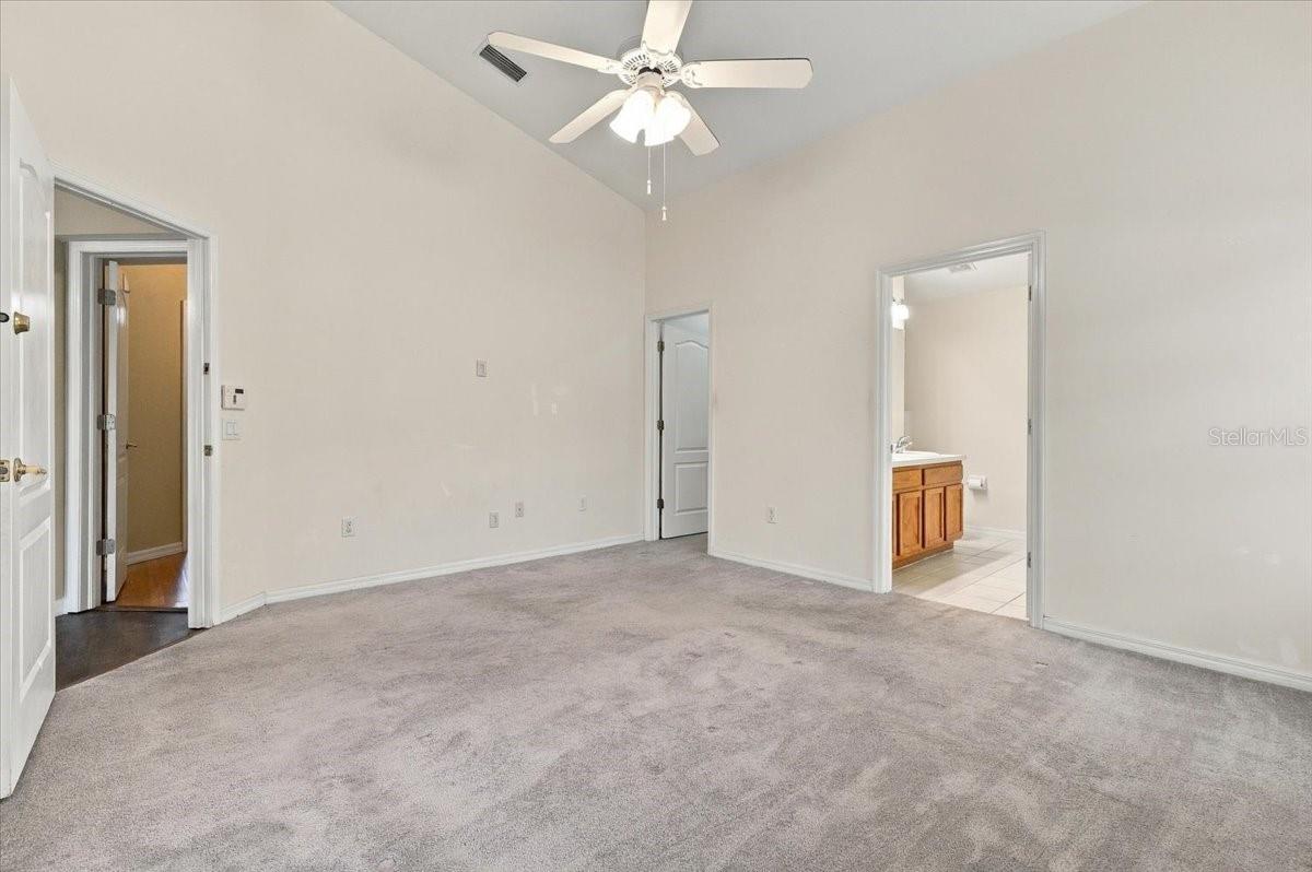 Empty carpeted bedroom with a ceiling fan and an open doorway to the bathroom.