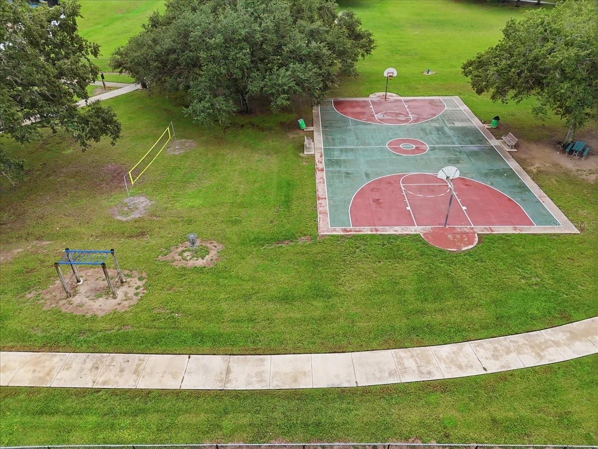 Aerial view of a neighborhood basketball court beside a grassy field and curved sidewalk.