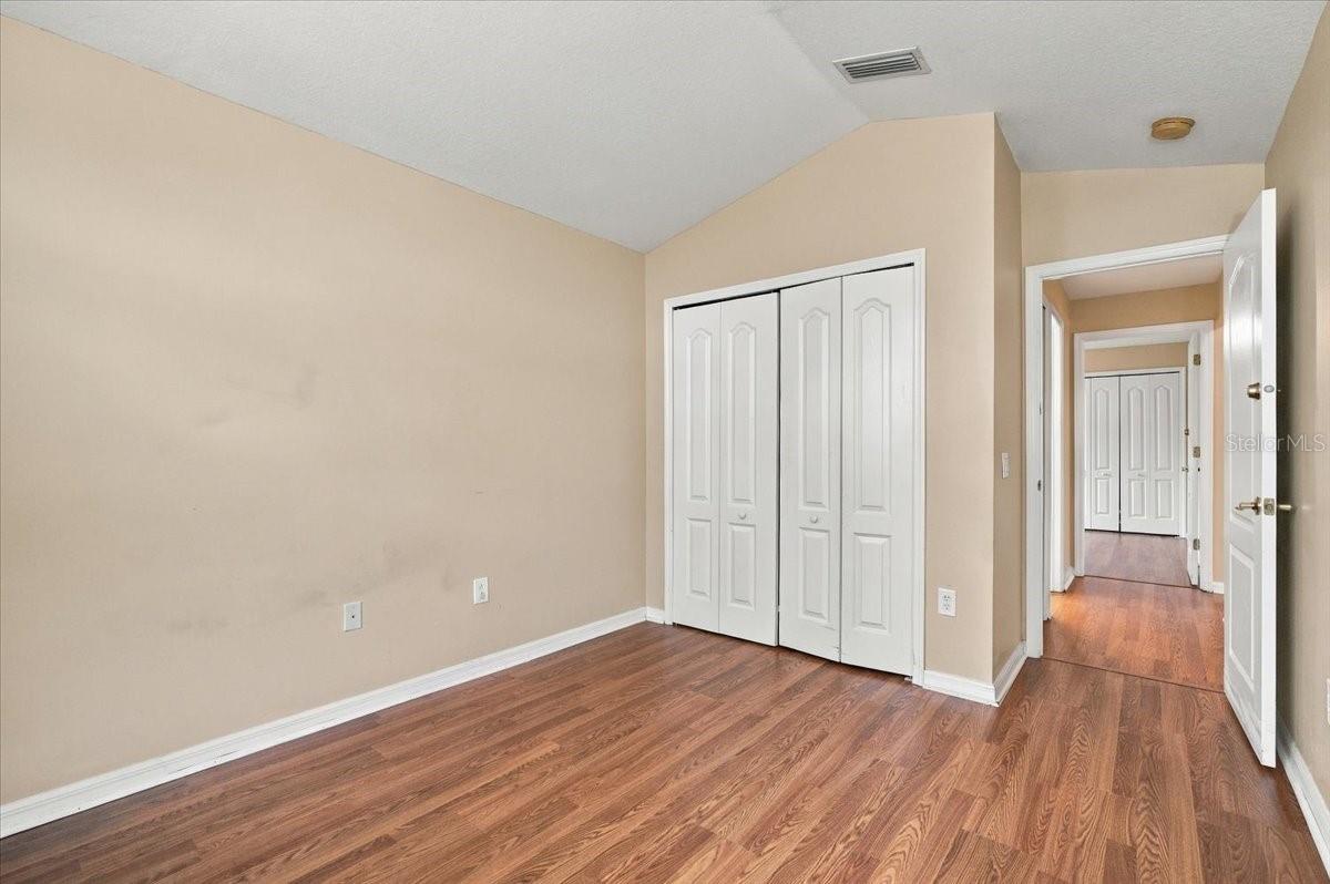 Empty bedroom with wood-look flooring, white closet doors, and an open doorway to the hall.