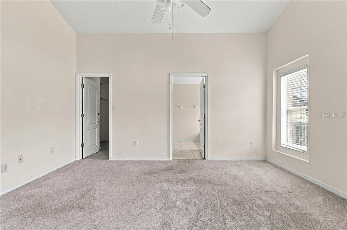 Empty carpeted bedroom with a ceiling fan, window, and two open doorways.