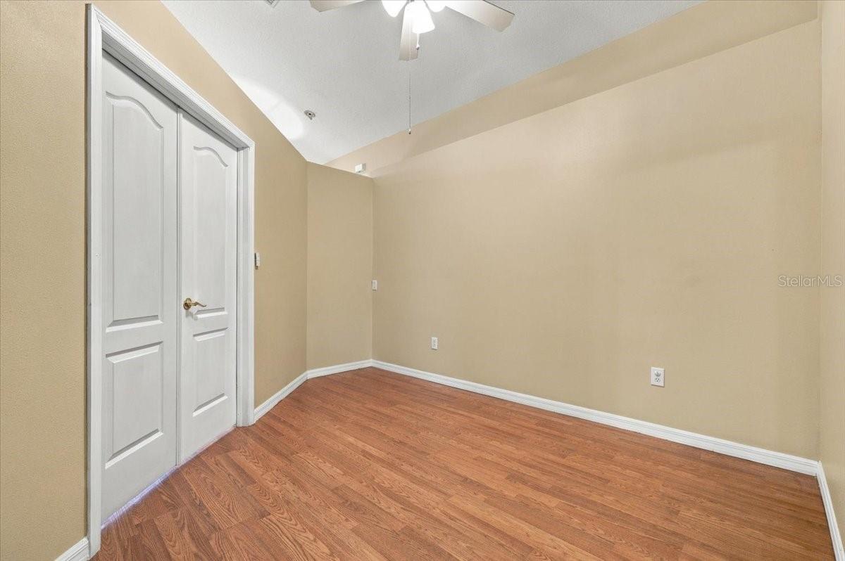 Empty room with tan walls, hardwood flooring, white double closet doors, and a ceiling fan.