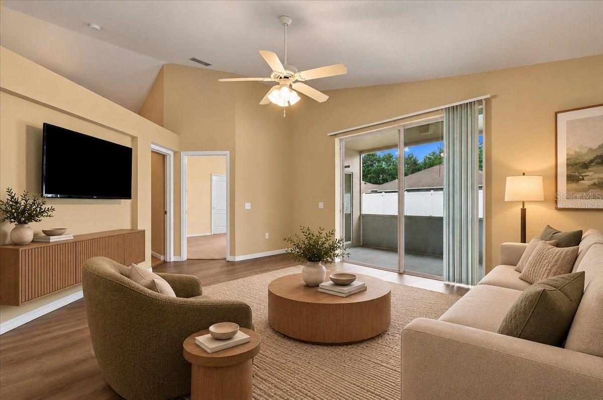 Virtually staged living room with a ceiling fan, sliding glass doors, and neutral furnishings.