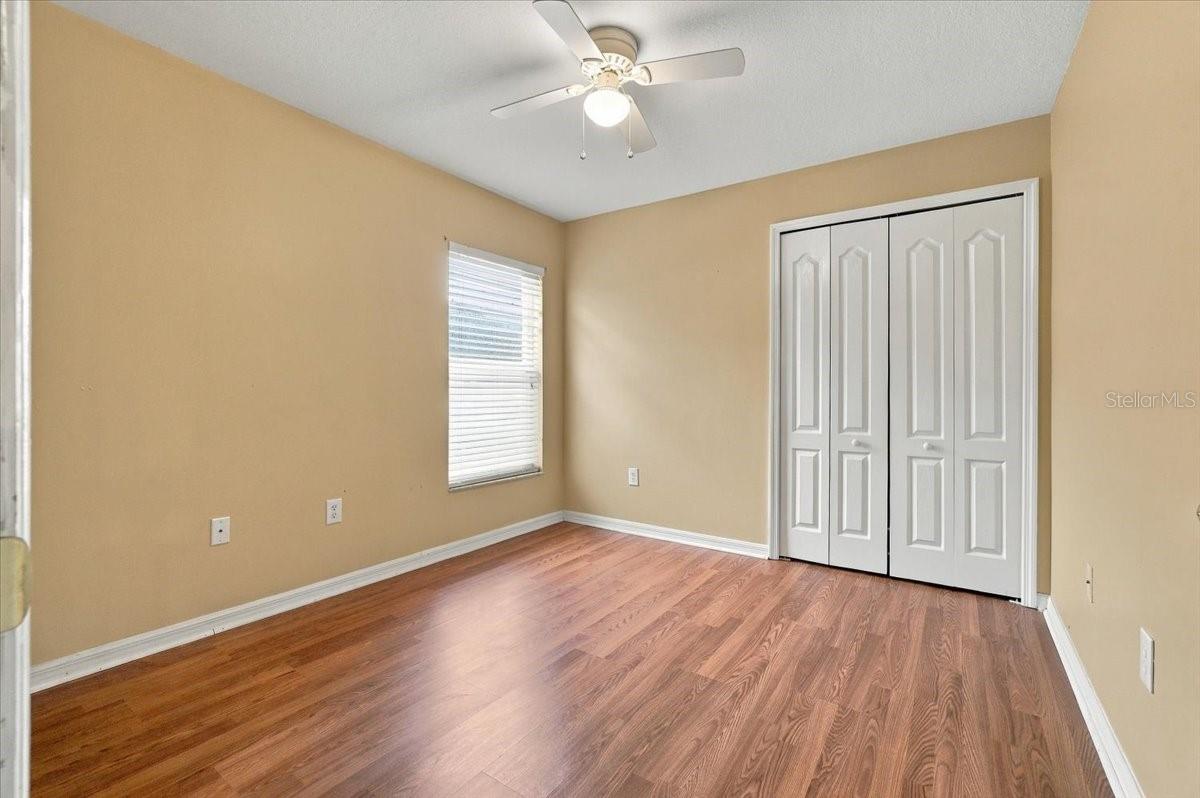 Empty bedroom with wood flooring, a window, and white closet doors.