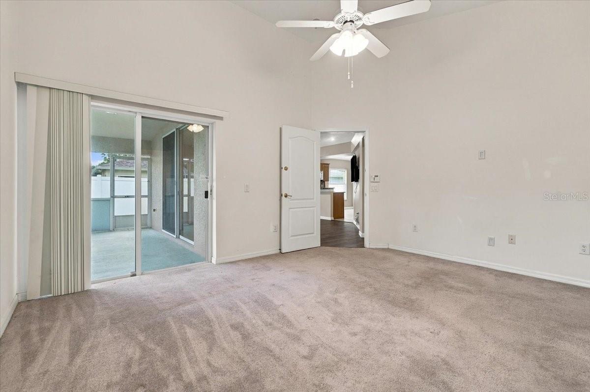 Empty carpeted room with a ceiling fan and sliding glass doors to an enclosed patio.