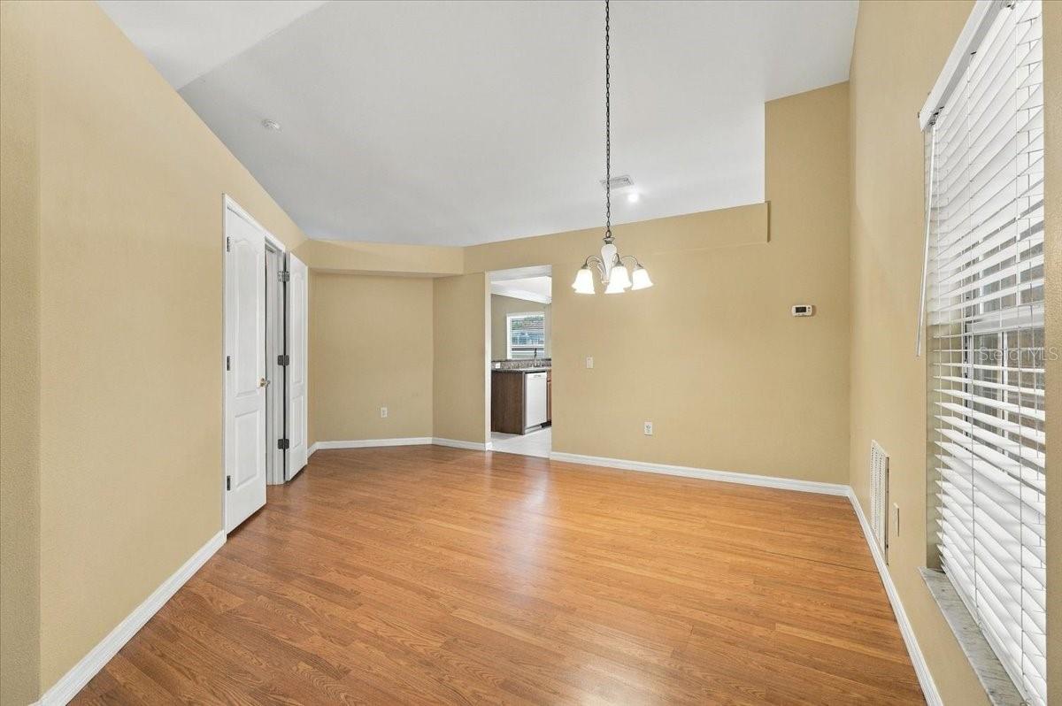 Empty dining room with hardwood floors, a hanging chandelier, and a large window with blinds.