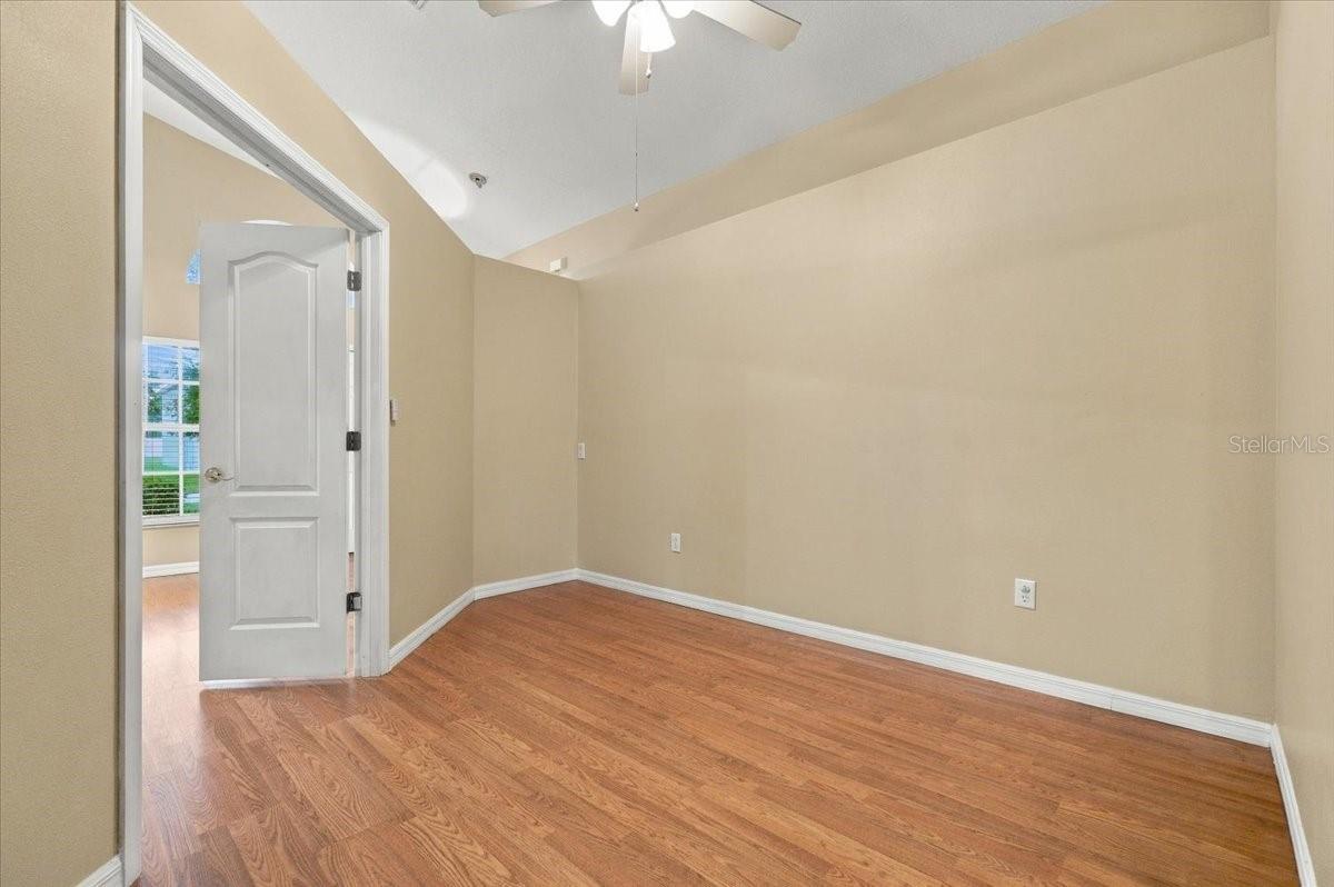Empty room with hardwood floors, beige walls, a ceiling fan, and an open doorway.