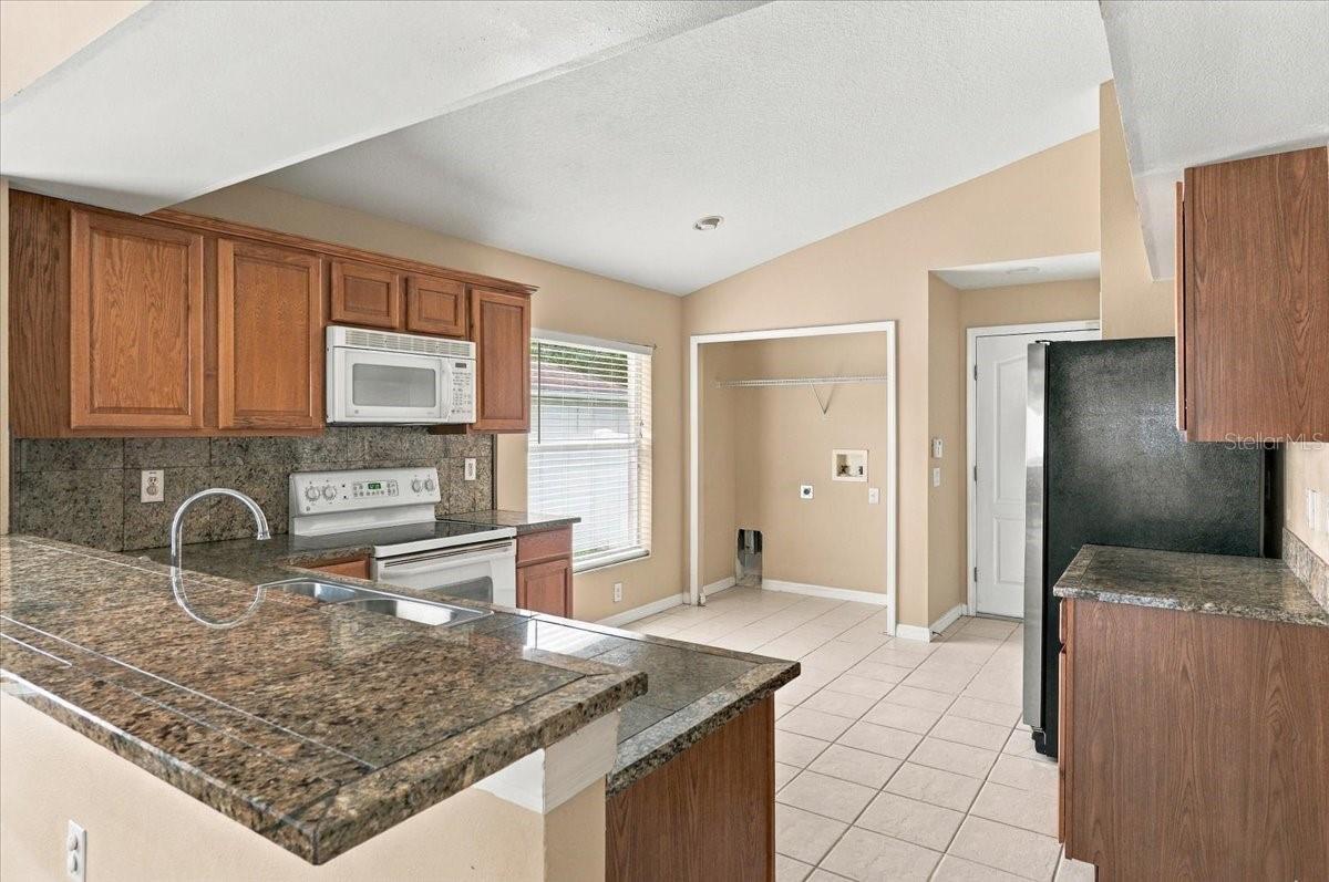 Kitchen with granite counters, wood cabinets, white appliances, and a tiled floor.