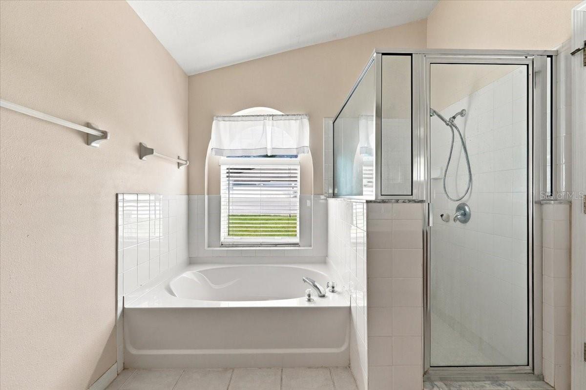 Bathroom with a built-in soaking tub beneath a window and a glass-enclosed shower.