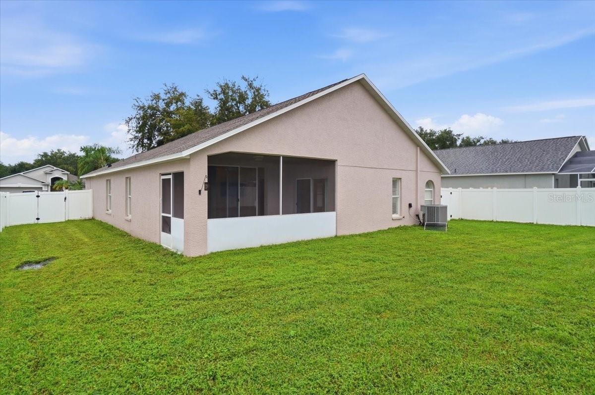 Rear exterior with screened lanai, broad green lawn, and white vinyl fencing.