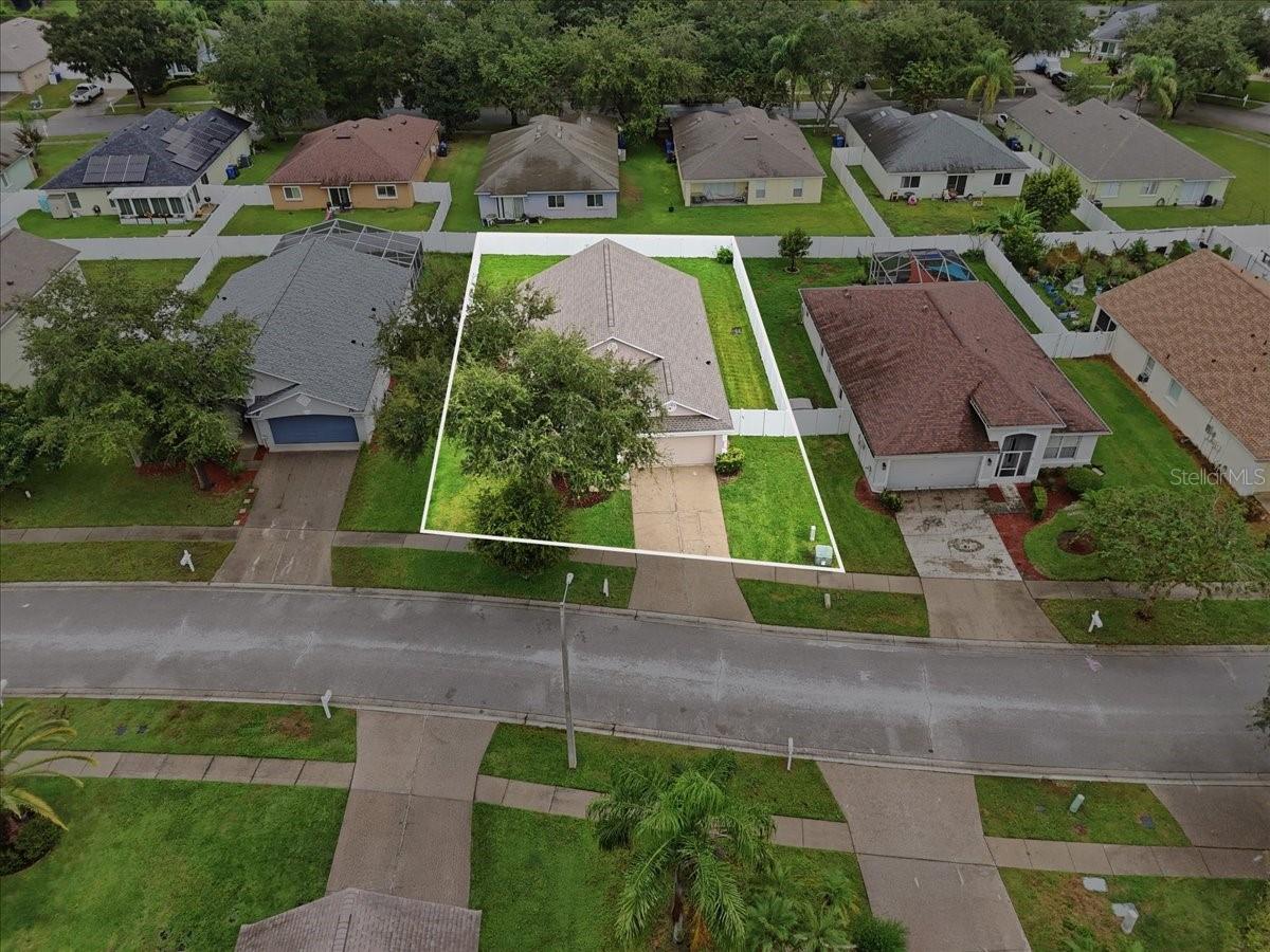 Aerial view of a single-story home and its outlined lot in a tree-lined neighborhood.