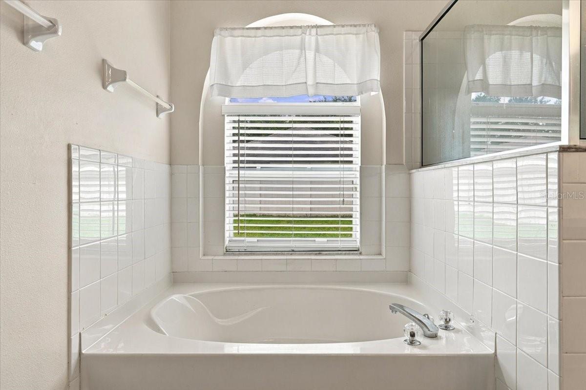 Corner bathtub beneath a curtained window, with white tile and chrome fixtures.