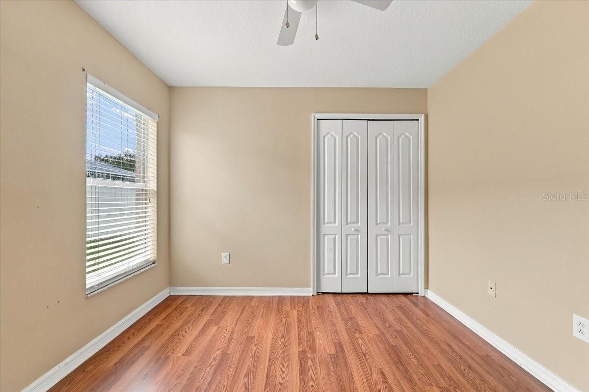 Empty bedroom with a window, double closet doors, and reddish wood-look flooring.
