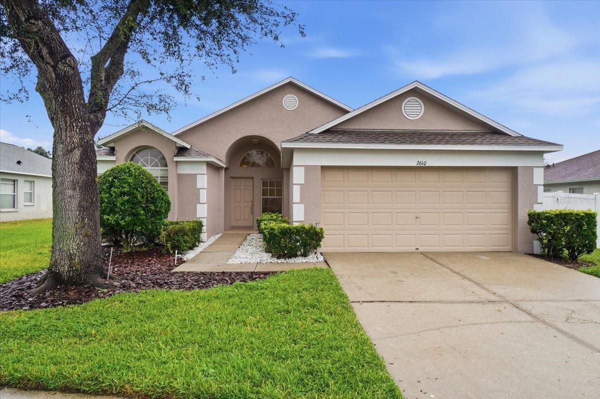 Single-story home with a two-car garage, arched entry, and large front-yard tree.