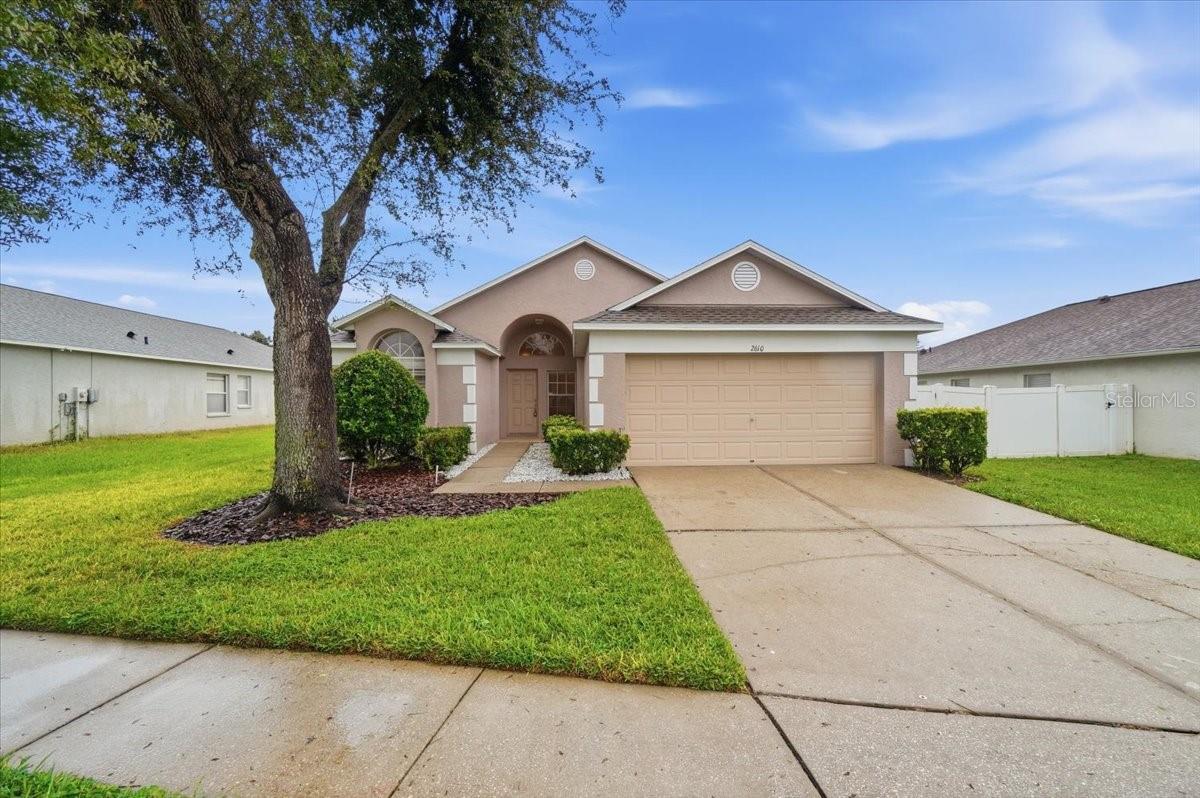 Single-story home with a large double garage, arched entry, and mature front-yard tree.