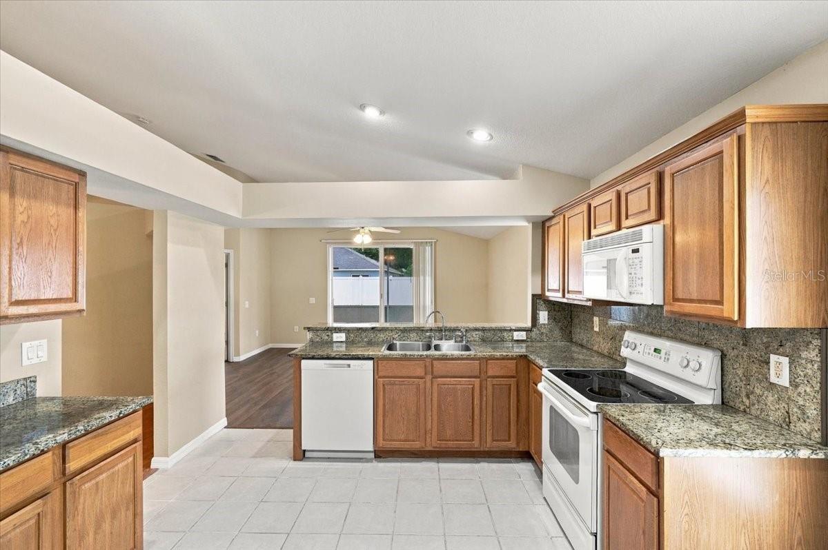 Kitchen with wood cabinets, granite counters, and white appliances opening to a dining area.