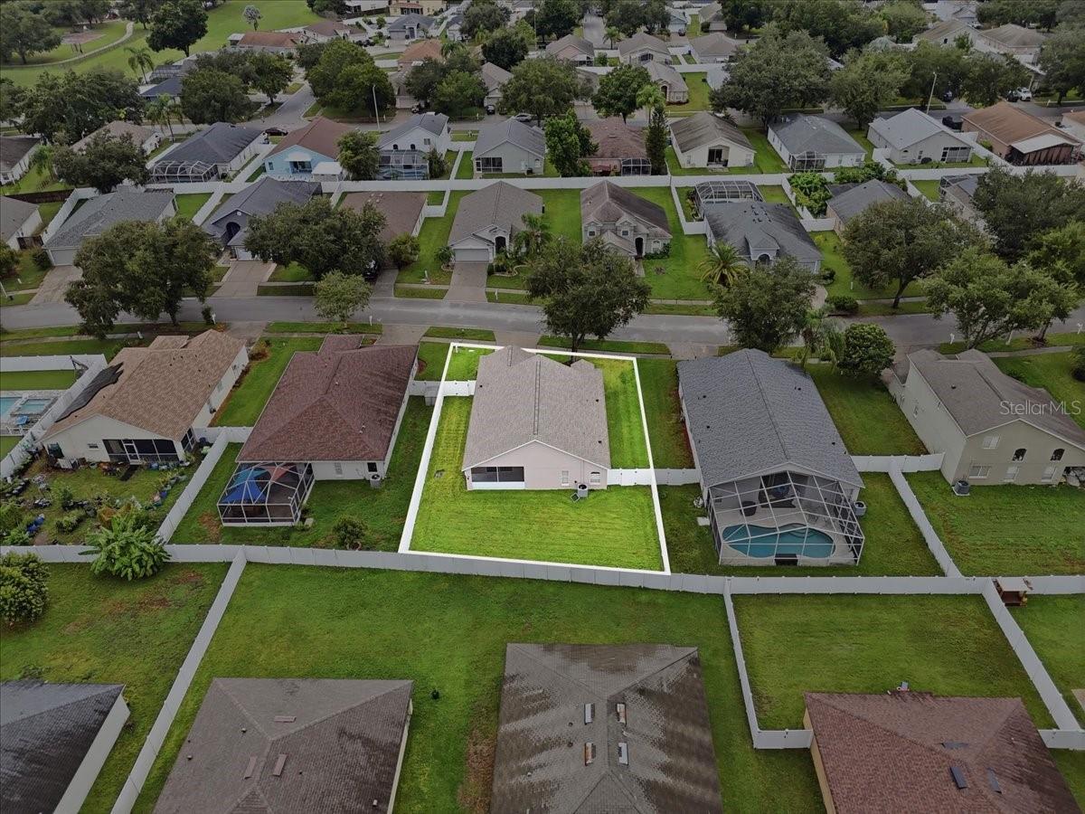 Aerial view of a single-story home and fenced yard outlined among neighboring homes.