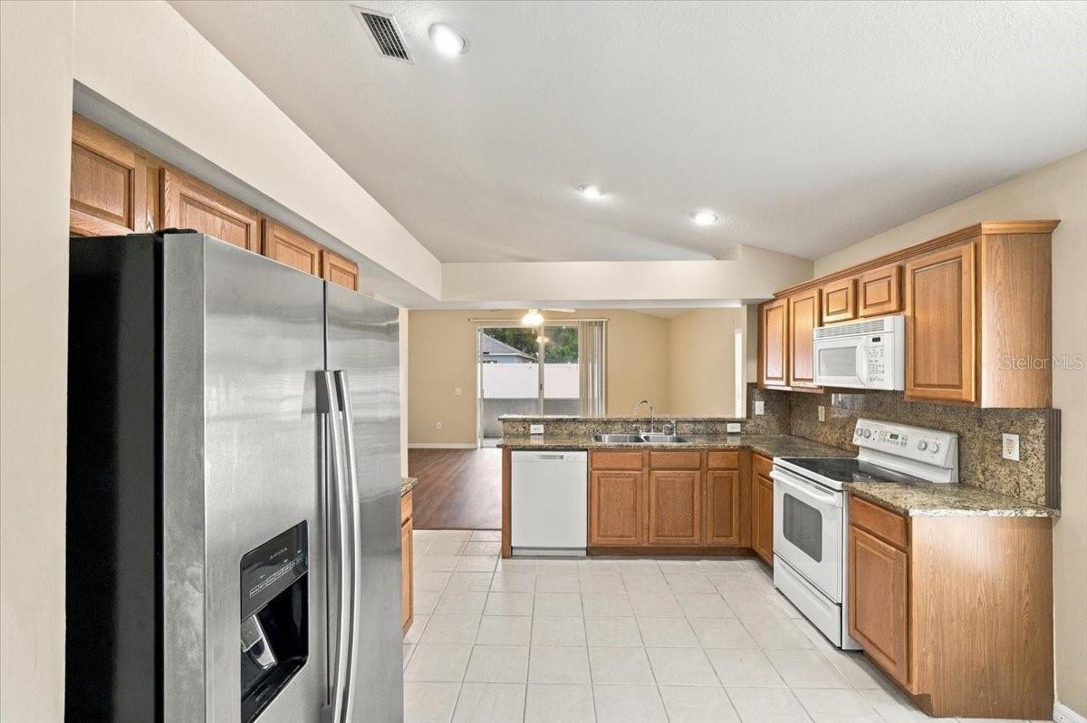 Kitchen with wood cabinets, granite counters, stainless refrigerator, and white appliances.