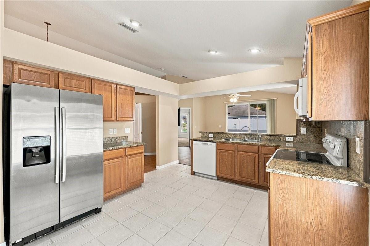 Kitchen with wood cabinets, granite countertops, stainless steel refrigerator, and tile flooring.