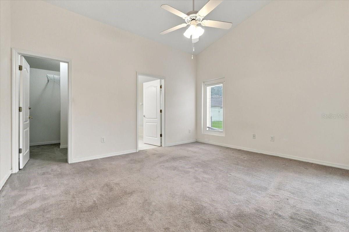 Vacant bedroom with gray carpet, a ceiling fan, and an open closet.