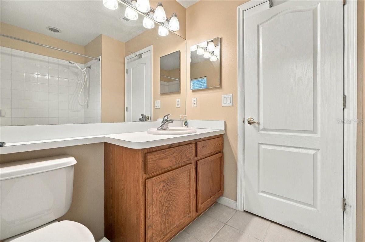 Bathroom with a wood vanity, wide mirror, toilet, and tiled tub-shower.