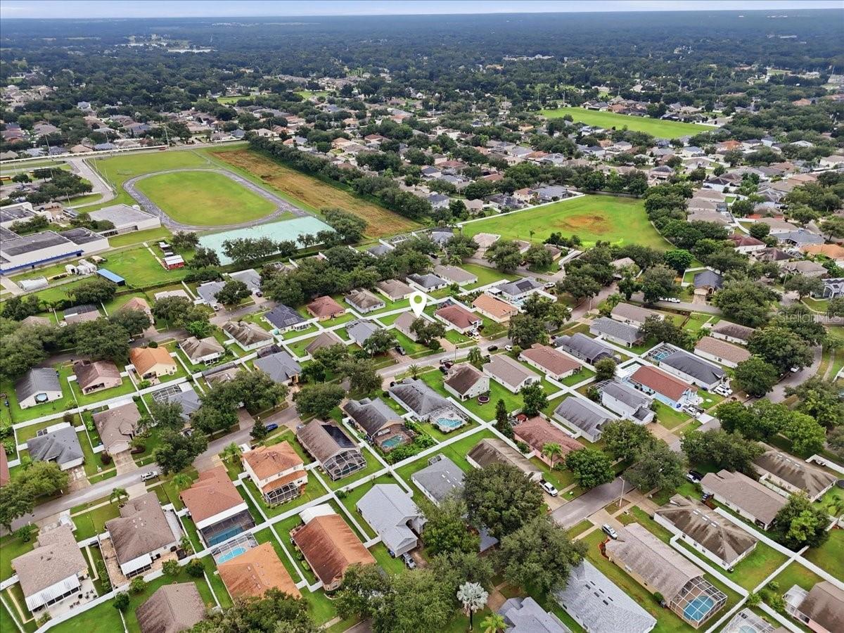 Aerial view of a suburban neighborhood with a green field and the property marked by a pin.