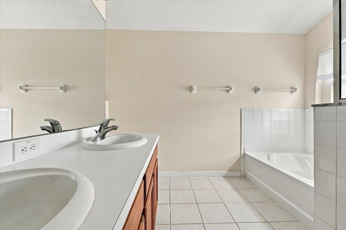 Bathroom with a double-sink vanity and a white-tiled bathtub.