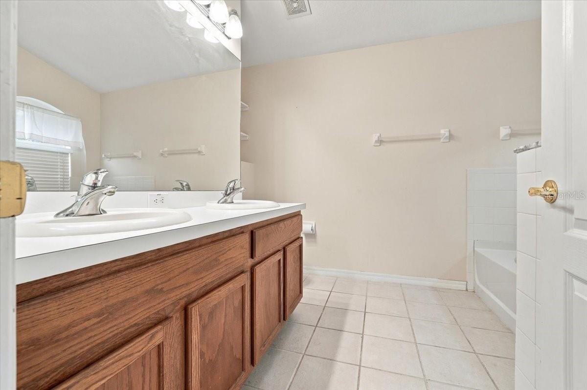 Bathroom with a double-sink wood vanity, large mirror, and tiled bathtub.