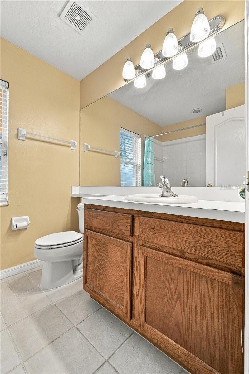 Bathroom with a large mirror, wood vanity, white sink, and toilet.