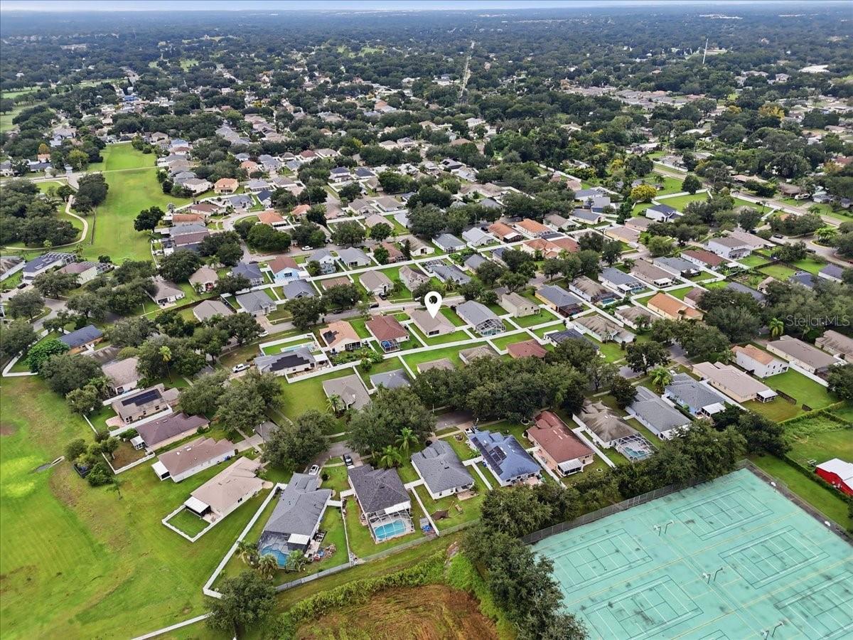 Aerial view of a tree-lined neighborhood with a location marker and tennis courts.