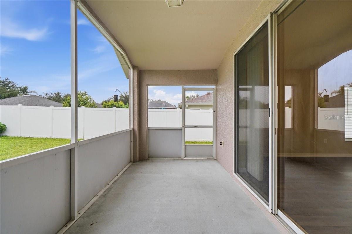 Screened-in patio with a concrete floor, sliding glass doors, and a white fenced yard beyond.