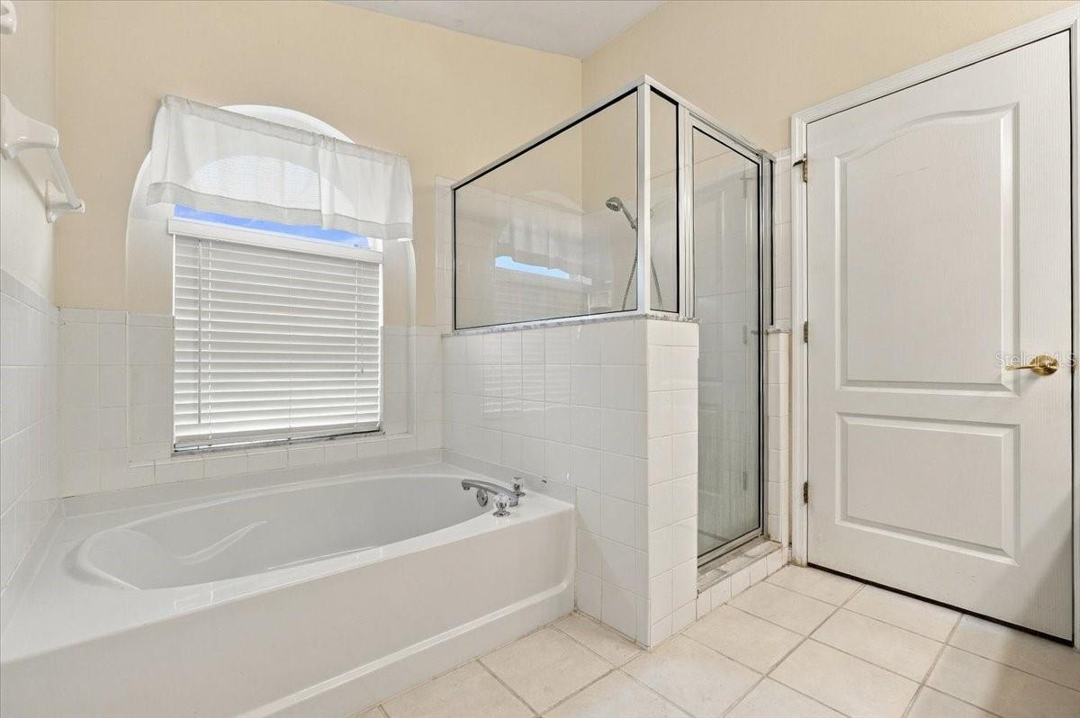 Bathroom with a built-in soaking tub and glass-enclosed shower beside a window with blinds.
