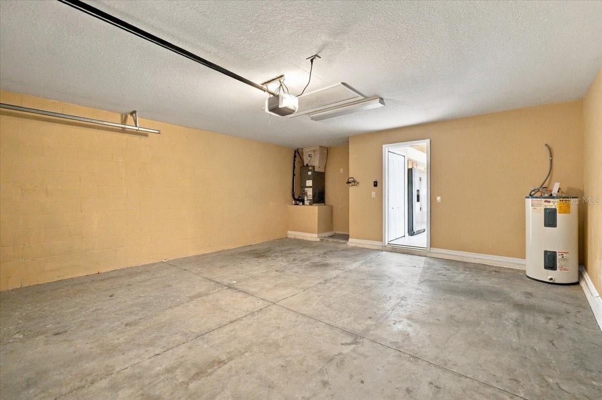 Empty two-car garage with a concrete floor, water heater, and automatic garage door opener.