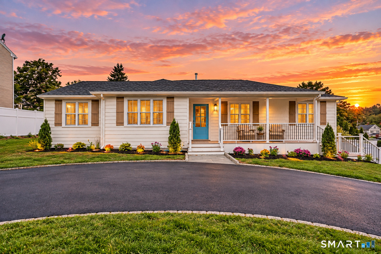 White single-story house with a teal front door and covered porch at sunset.