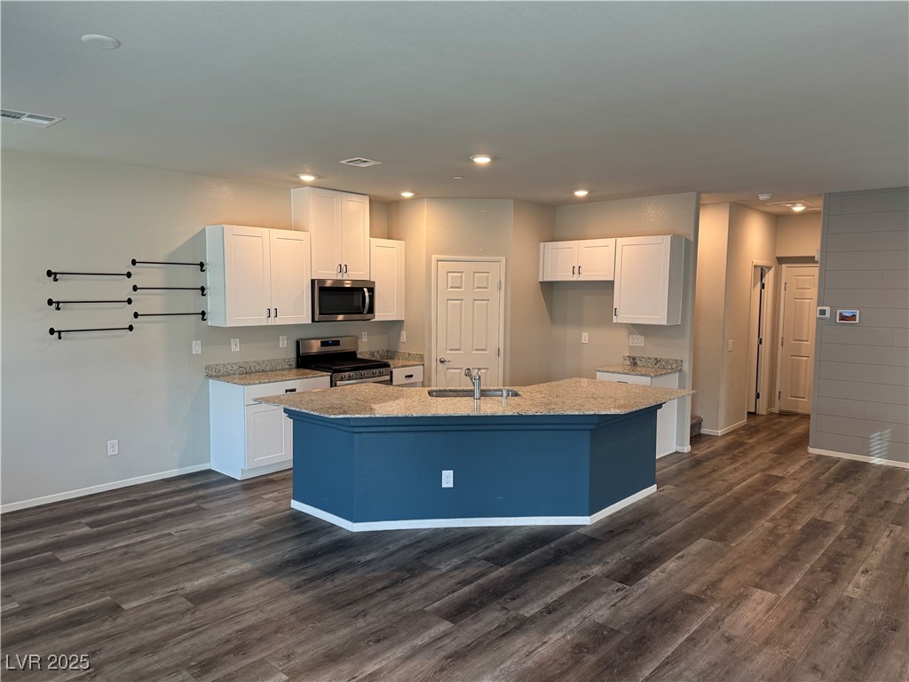 Open kitchen with a blue peninsula island, white cabinets, granite counters, and dark wood-look flooring.
