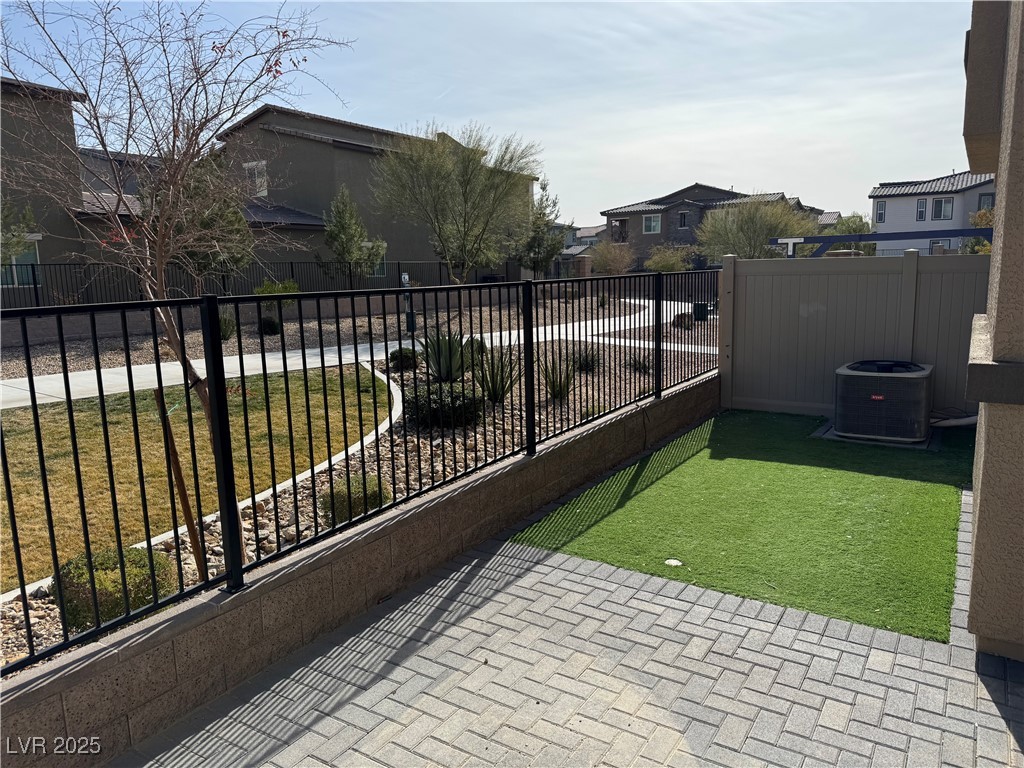 Backyard patio with artificial turf, paver flooring, and a black metal fence beside a landscaped walkway.