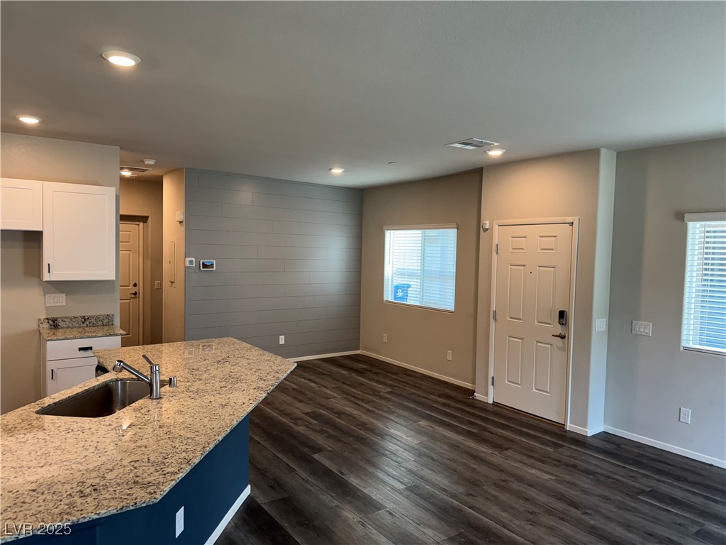 Unfurnished open-plan kitchen and living area with a granite peninsula and gray accent wall.