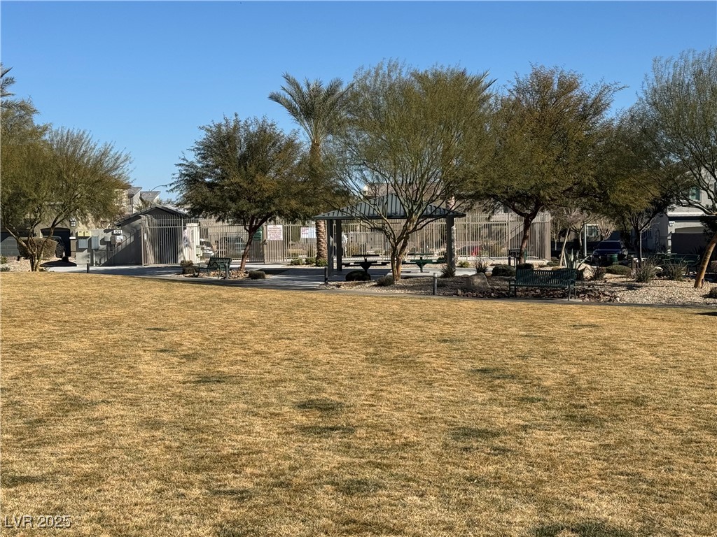 Community lawn with shade trees, benches, and a covered gazebo beside a fenced area.
