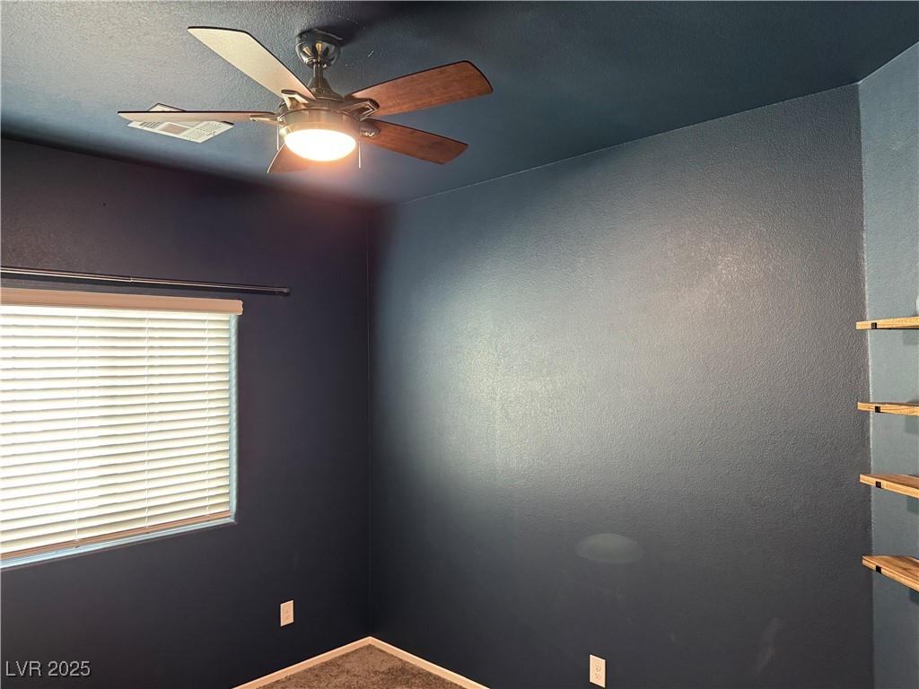 Vacant room with dark walls, carpet, a window with blinds, ceiling fan, and wooden shelves.